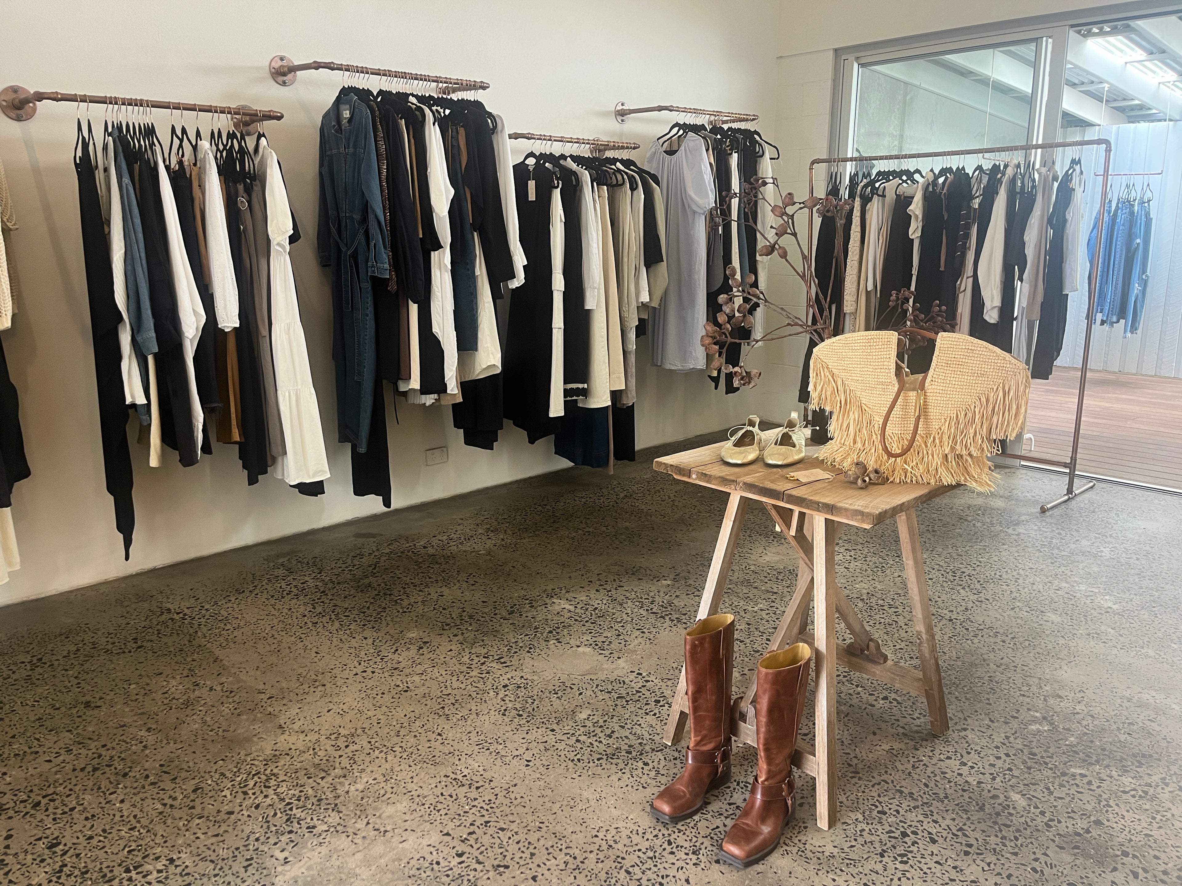 Clothing store interior with racks of clothes and a table with boots and bags.